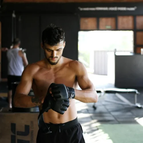 Photo by Bruno Bueno Shirtless man preparing for an intense workout session in a gym, wearing boxing gloves.