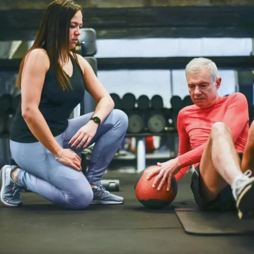 Photo by Kampus Production A senior man exercising with a personal trainer in a gym, focusing on core workouts.