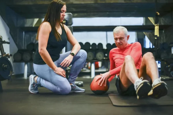 Photo by Kampus Production A senior man exercising with a personal trainer in a gym, focusing on core workouts.